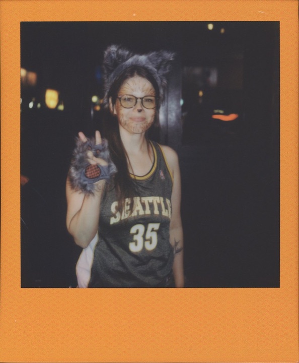 Polaroid of Birdie in fuzzy ears and face paint, making a peace sign
